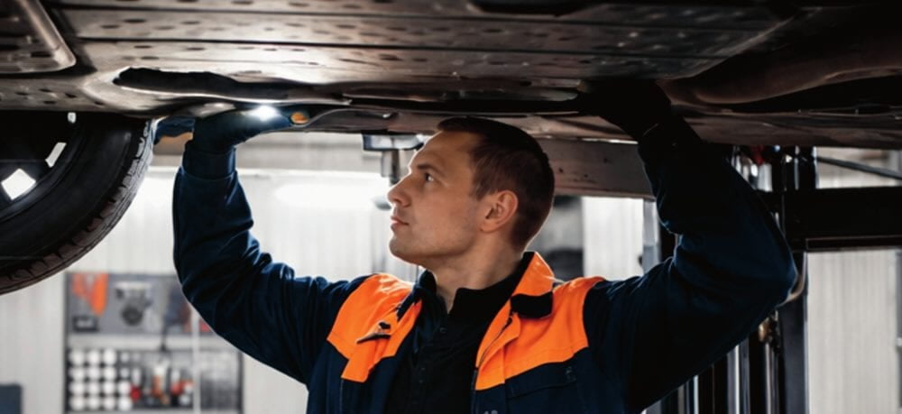 Herpel Lift technician inspecting the underside of a vehicle on a lift
